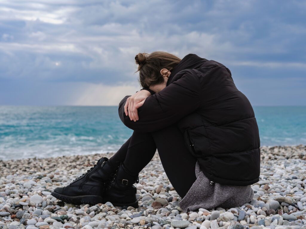 pexels-photo-10817191-10817191 A woman sitting on a rocky beach, expressing solitude and contemplation by the sea.